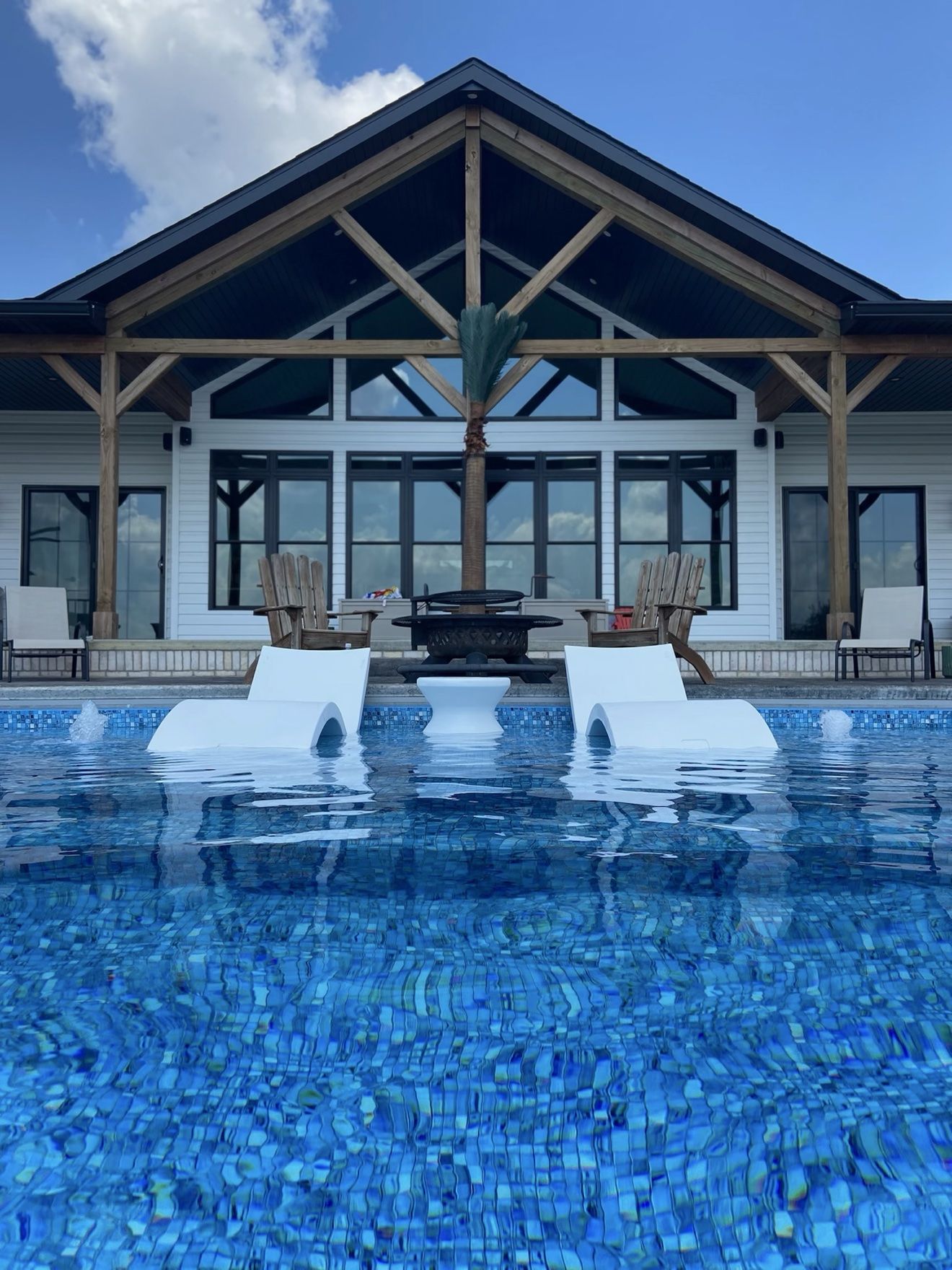 Inground pool with tanning ledge, in-pool loungers and bubblers built by Fattys Pools in front of a pool house