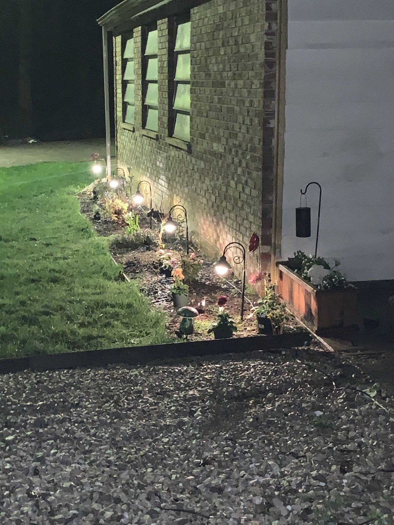 Lighted landscape bed at night from another angle, with a wooden planter box