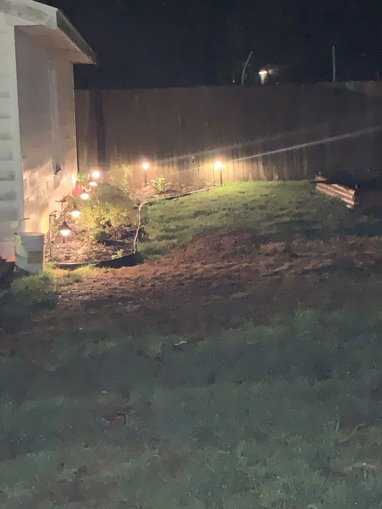 Lighted landscape bed along a backyard fence at night