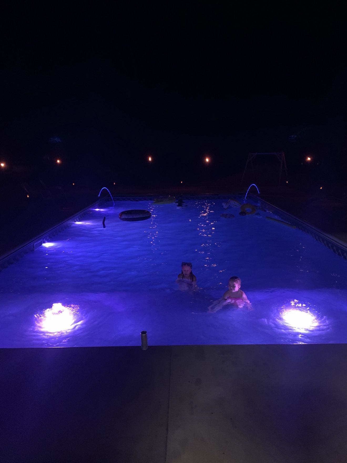 Kids night swimming in the glowing pool with the tanning ledge lit and bubblers running