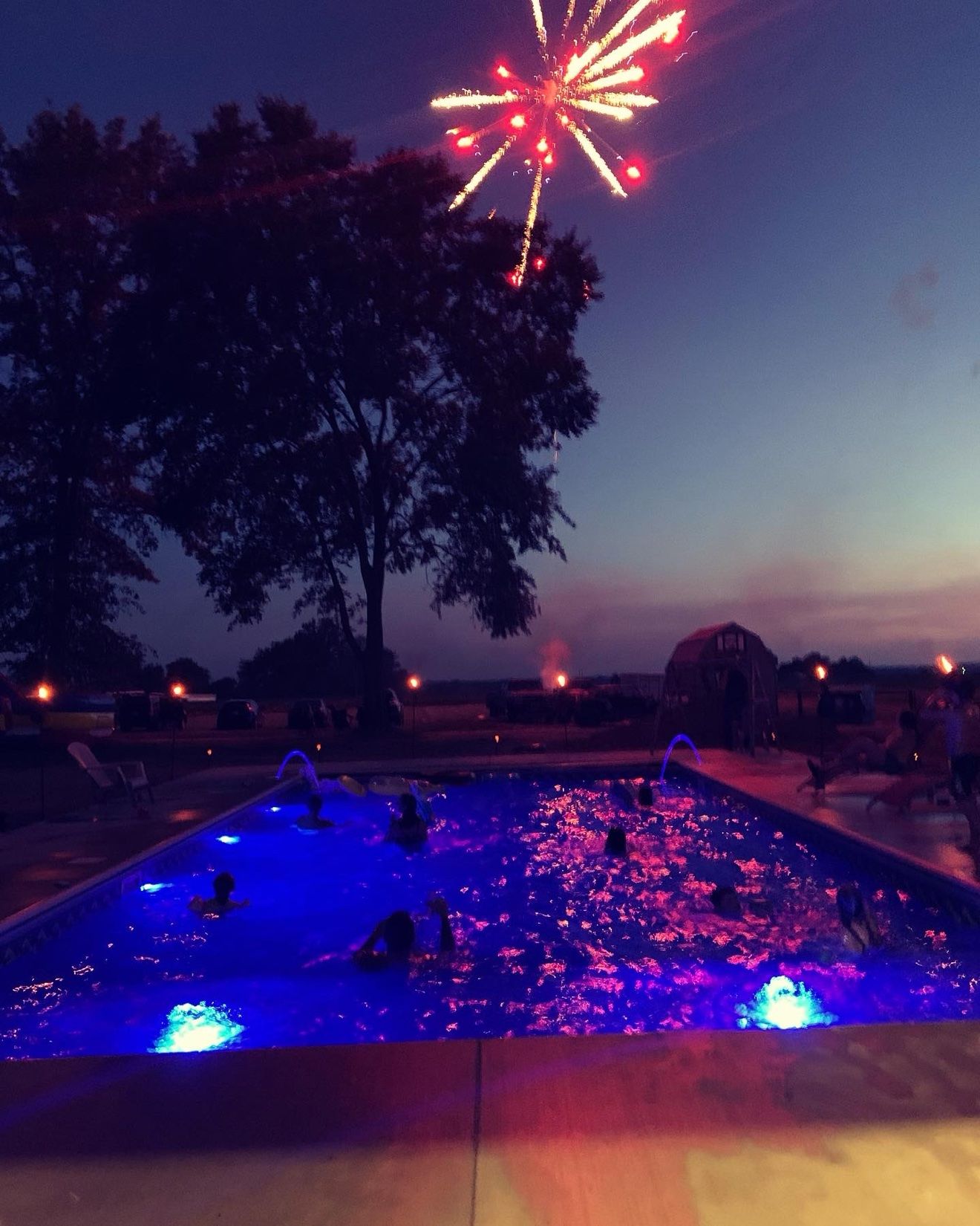 Red fireworks bursting over the pool, lit blue and pink by its LED lights